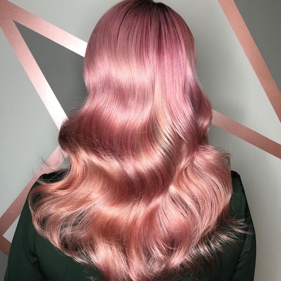 A person with glossy pink, wavy hair facing a gray and pink colored wall