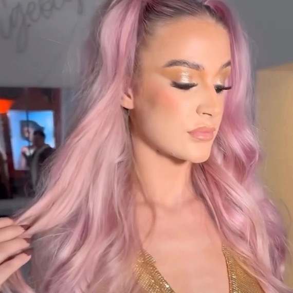 A headshot of a person with long light pink hair looking down