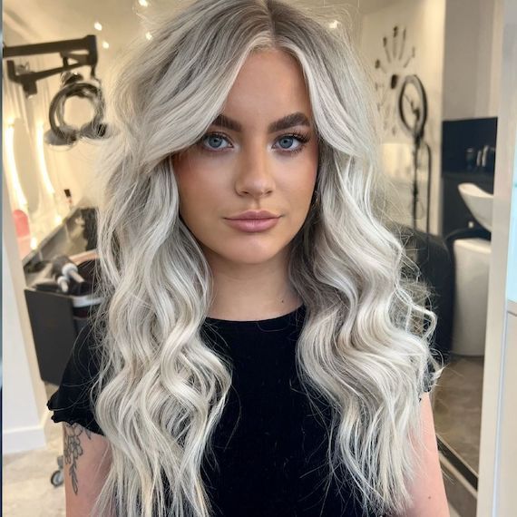 Model with tousled hair and platinum blonde highlights faces camera.