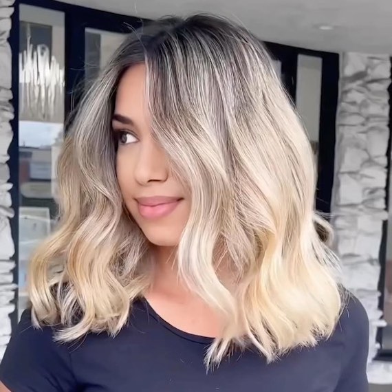 Side profile of model with mid-length, wavy hair, featuring dark roots and platinum ombre lengths.
