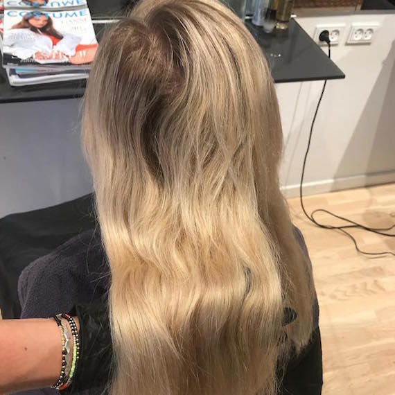 Back of woman’s head with long, blonde hair and dark roots.
