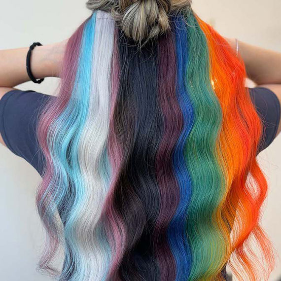 Model’s long, wavy hair is painted in colors from the Progress Pride flag, including pastel tones and bold brights.