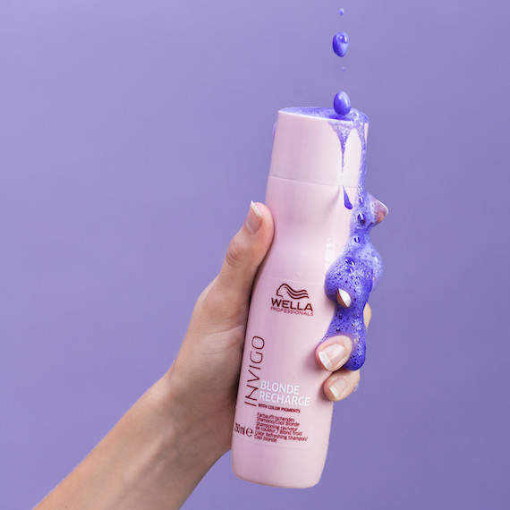 Close up of hand holding a bottle of Wella INVIGO Blonde Recharge purple shampoo