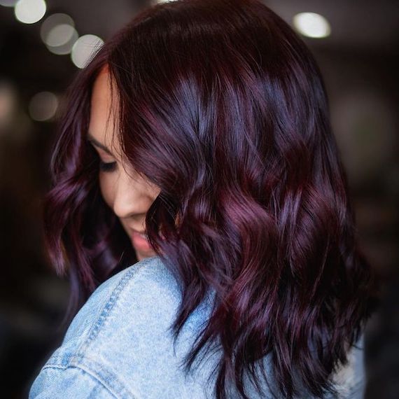 Model with loosely curled hair and purple balayage glances over shoulder.