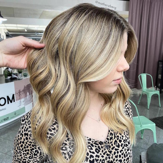 Hand tousling wavy, blonde hair in Wella Professionals salon.