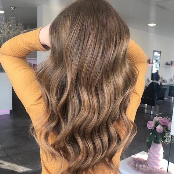 Photo showing back of woman’s head as she swishes long, brown wavy hair in a Wella Professionals salon.