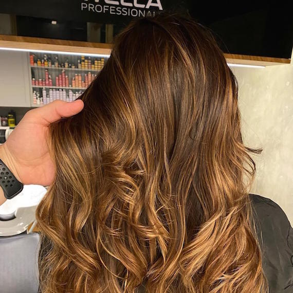 Hand tousling wavy, brown hair in Wella Professionals salon.