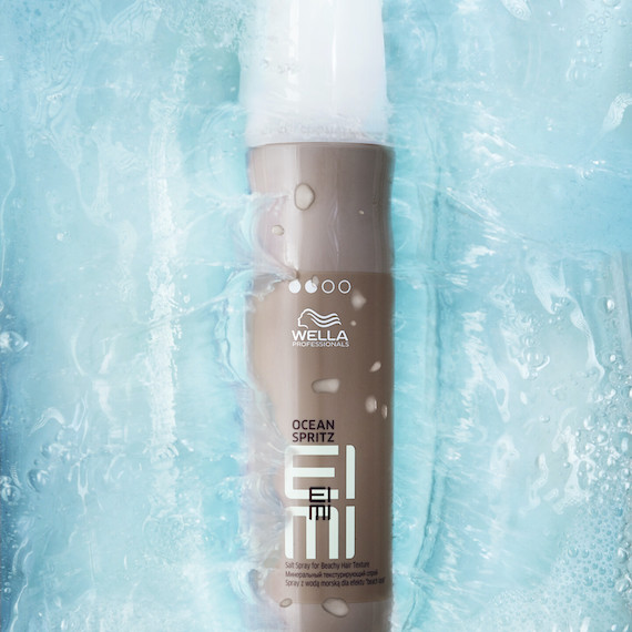 Eine Flasche EIMI Ocean Spritz Salzspray von Wella Professionals, die aus einem Wasserbecken auftaucht