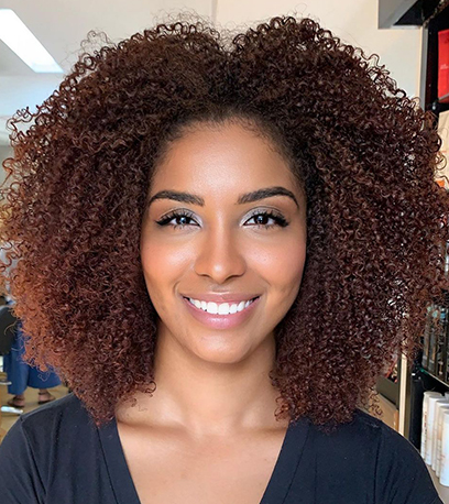 Headshot of a person with very curly brown hair that’s been cared for using Fusion products by Wella Professionals