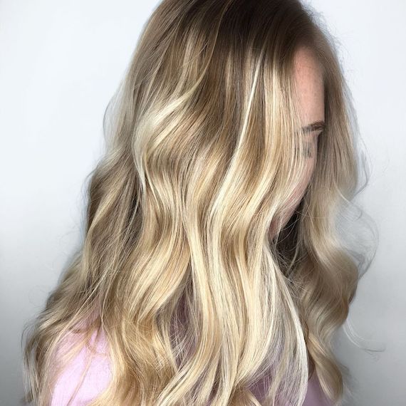Frau mit langem, blondem Balayage und dunklem Haaransatz, kreiert mit Wella Professionals.
