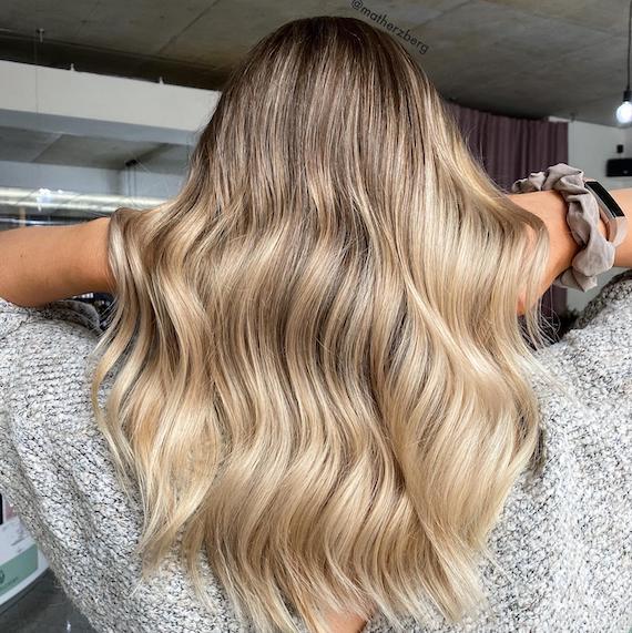 Frau mit cremeblondem Haar und dunklem Ansatz, kreiert mit Wella Professionals.
