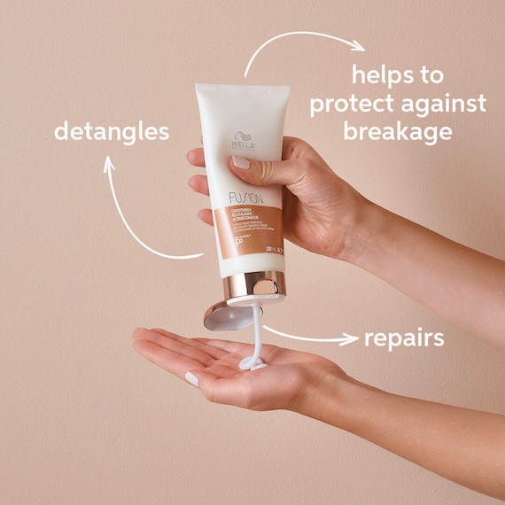 Close-up of a person squeezing a bottle of Fusion Intense Repair Conditioner by Wella Professionals into their palm