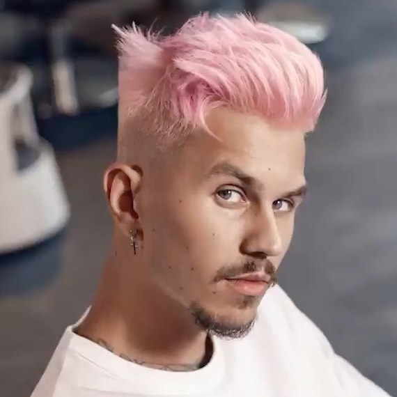 Ein Model mit kurzem, pastellrosa Haar, das zu einer Tolle frisiert ist, schaut in die Kamera.