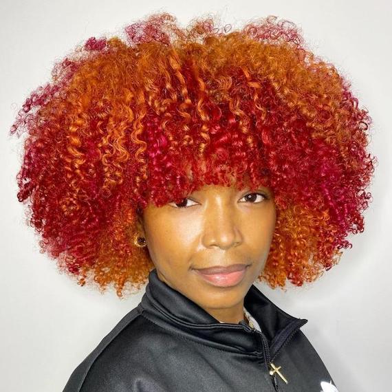 Ein Model mit mittellangem, lockigem rotem und orangefarbenem Haar lächelt in die Kamera.