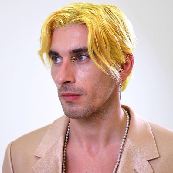 Ein Model mit kurzem, mittig gescheiteltem, neongelbem Haar schaut von der Kamera weg.
