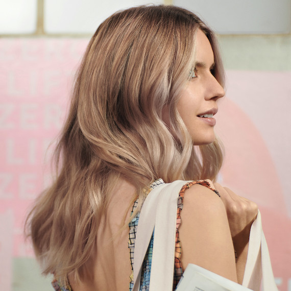 Side profile of model with long, wavy, glossy, ash blonde hair.