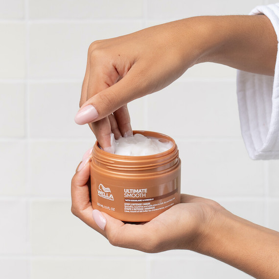 Model reaches into a tub of ULTIMATE SMOOTH Mask.