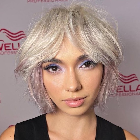 Model with blonde ‘bixie’ (bob pixie) haircut looks directly into camera.