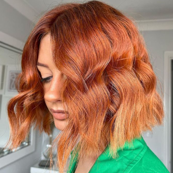 Model with shoulder-length, wavy, copper hair that fades lighter on the ends.