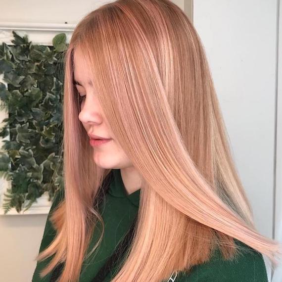 Frau mit grünem Hemd und hellen erdbeerblonden Strähnchen, die mit Wella Professionals kreiert wurden.