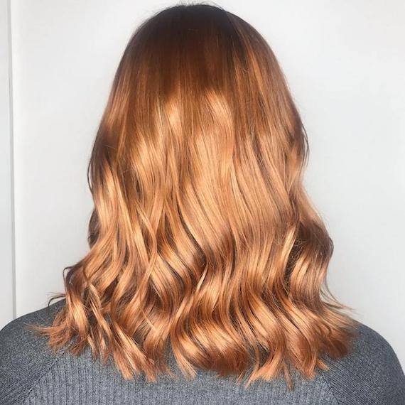 Hinterkopf einer Frau mit mittellangem, gewelltem, erdbeerblondem Balayage, kreiert mit Wella Professionals.