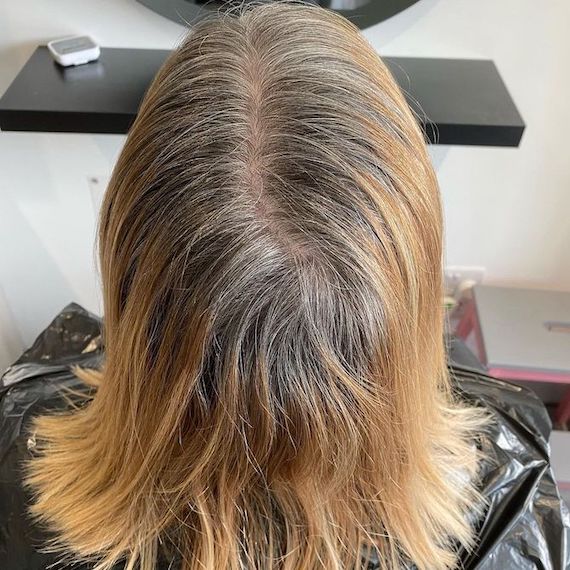 Back of woman’s head with blonde hair and grown-out gray roots.