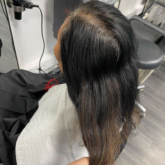 Back of woman’s head with long, black hair and grown-out gray roots.