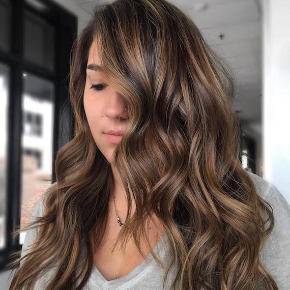 Model with long, dark brown, wavy hair and subtle highlights, created using Wella Professionals.