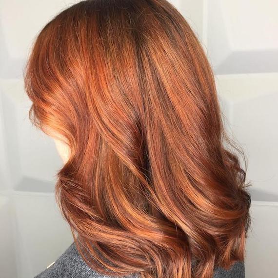 Model with mid-length, red, wavy hair and subtle copper highlights, created using Wella Professionals.