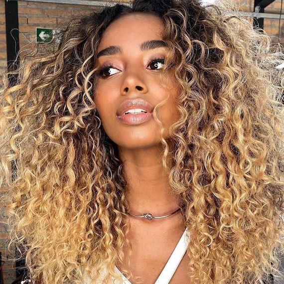 Model with long, curly, golden blonde hair and dark roots.