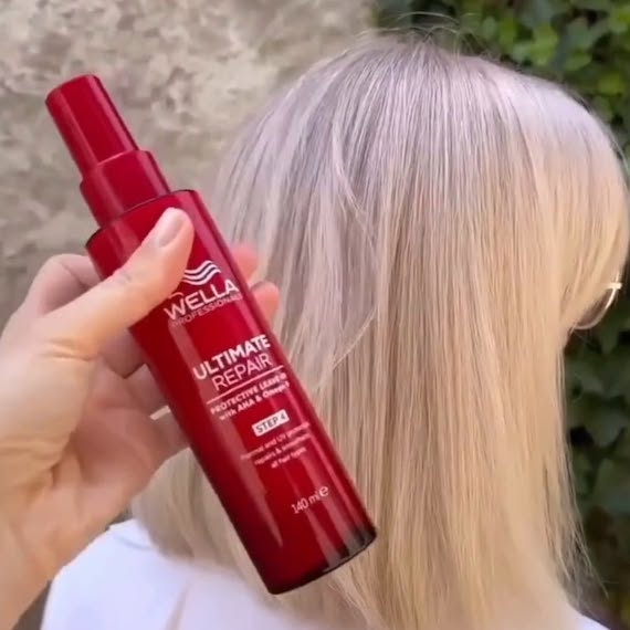 ULTIMATE REPAIR Protective Leave-In is held in front of a model’s straight, blonde hair.