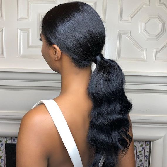 Model with long, dark hair styled in a low-slung, loosely curled ponytail.