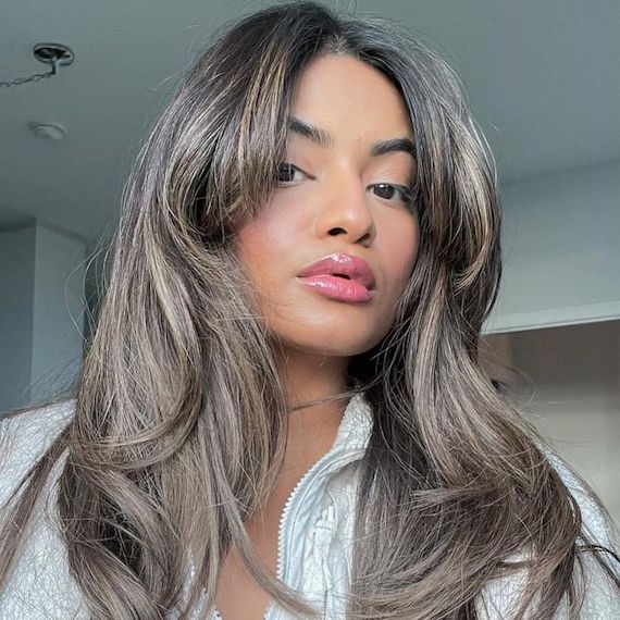 Model with long, dark hair featuring ash blonde highlights and a grown-out fringe.