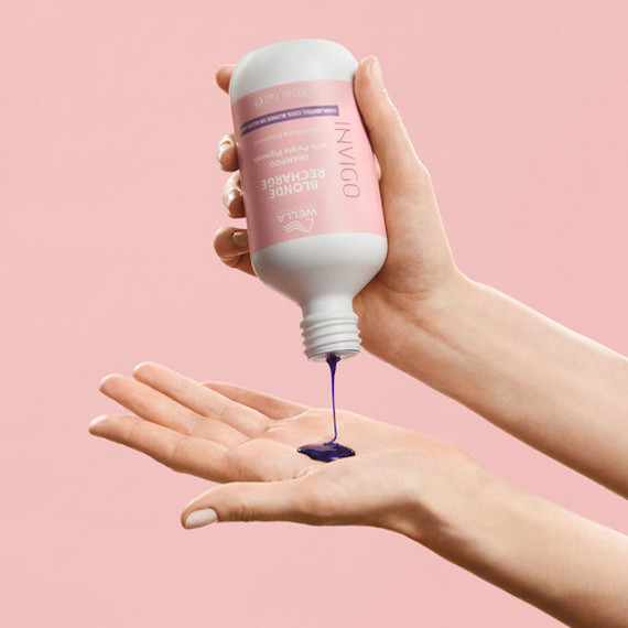 Model holds a bottle of INVIGO Blonde Recharge Shampoo, with the purple pigment pouring out.