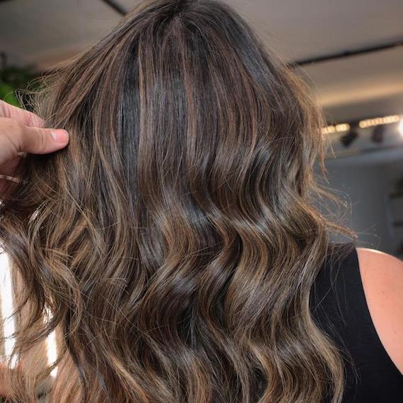 Back of woman’s head with long, wavy brunette hair and subtle twilights, created using Wella Professionals.