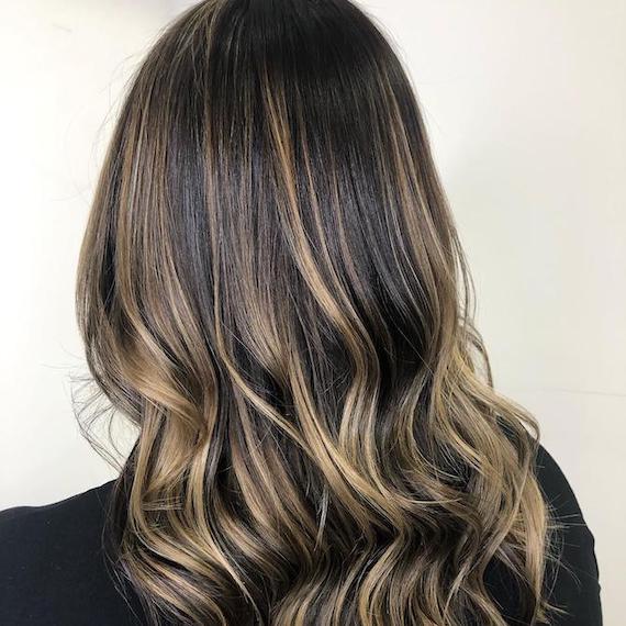 Back of woman’s head with long, wavy dark brunette hair and cool blonde twilights, created using Wella Professionals.