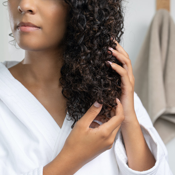 Model smooths ULTIMATE SMOOTH Miracle Oil Serum through their dark, curly hair.