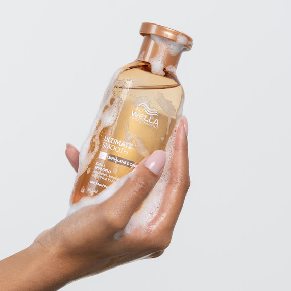 Model holds up bottle of ULTIMATE SMOOTH Shampoo.