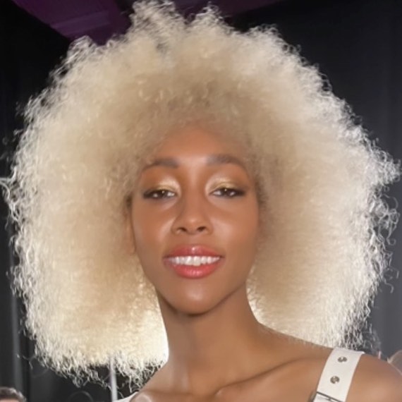 Model with voluminous, curly hair in a creamy vanilla blonde shade.