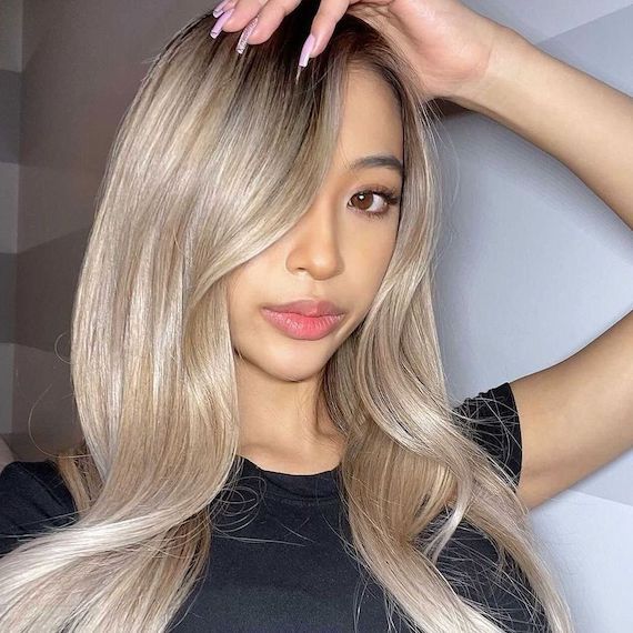 Model with long, rooted vanilla blonde hair styled in a glossy blow-dry.
