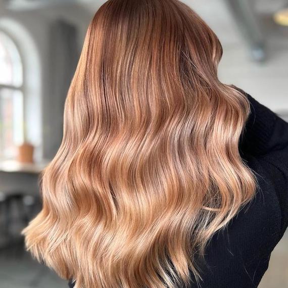 A person dressed in black faces away from the camera to show her wavy, walnut blonde hair