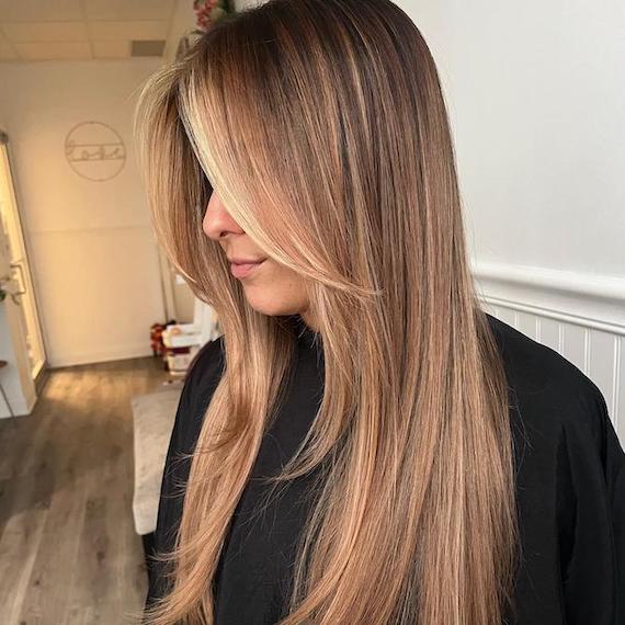 A person dressed in black faces the side. They have long walnut blonde hair