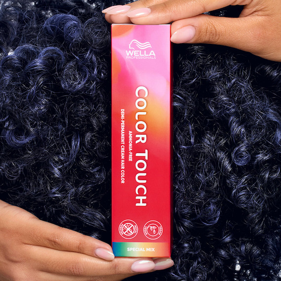 Model with curly, dark blue hair holding up a box of Color Touch.