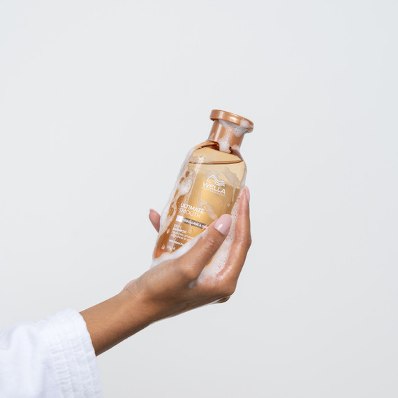 Model holds a bottle of ULTIMATE SMOOTH Shampoo.