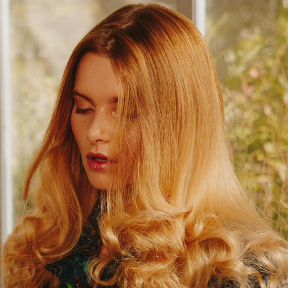 Close-up photo of model gazing downwards. Her golden blonde hair is styled in loose, lightly-tousled waves, by Wella Professionals Model gazing downwards. Her golden blonde hair is styled in loose, lightly-tousled waves.