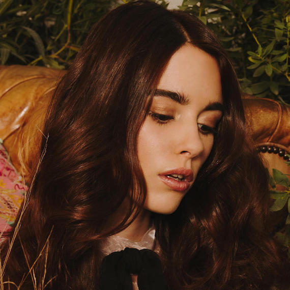 Close-up photo of model gazing downwards. Her dark brunette hair is styled in loose, lightly-tousled waves, by Wella Professionals Model gazing downwards. Her dark brunette hair is styled in loose, lightly-tousled waves.