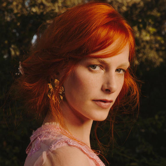 Model with red hair styled by Wella Professionals into a low, loose bun looks over her shoulder Model with red hair styled by Wella Professionals into a low, loose bun looks over her shoulder