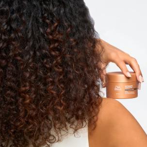 Model with long, curly, dark brown hair holds ULTIMATE SMOOTH Mask.