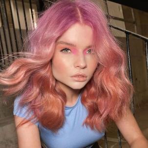 Model with wavy, pink and peach ombre hair faces the camera.