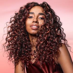 Model with long, dark brown, curly hair featuring coral highlights.